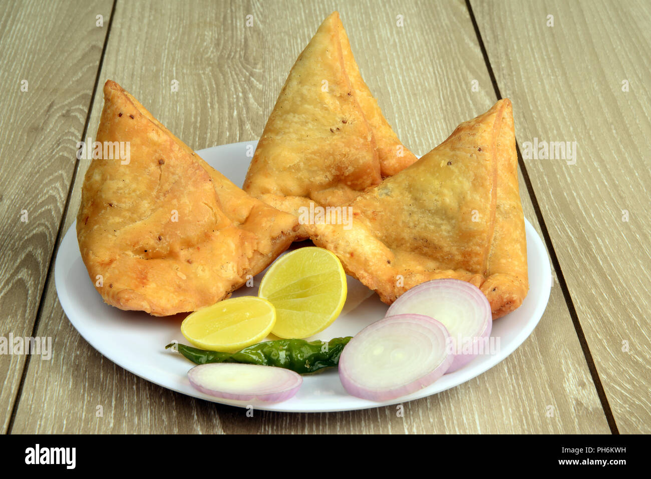 Punjabi Veg Samosa mit Zwiebel und Zitronenscheiben mit grünem Chili und Chutney auf hölzernen Hintergrund, Samosa ist ein beliebter Street Food in Indien Stockfoto