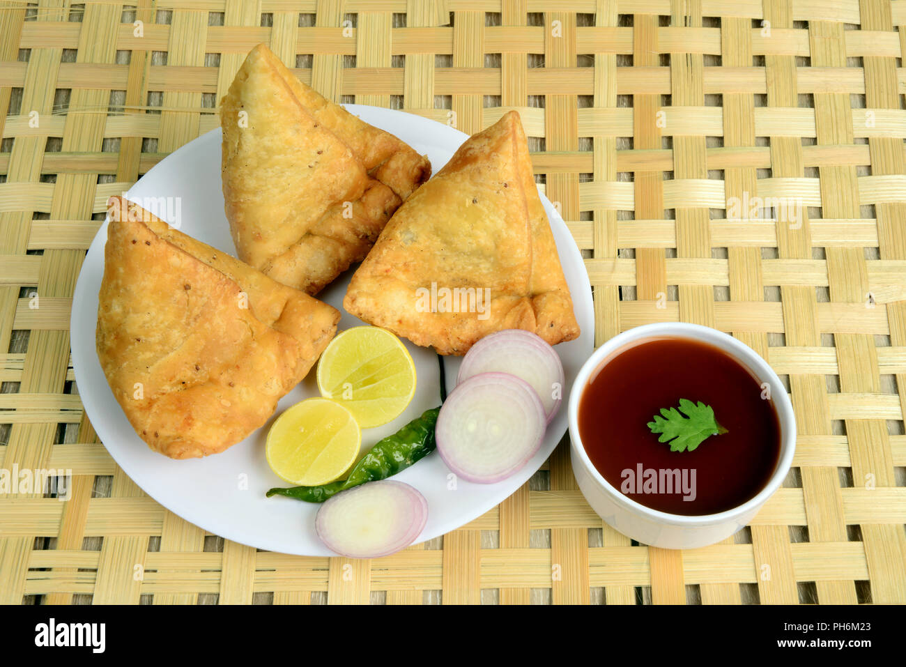 Punjabi Veg Samosa mit Zwiebel und Zitronenscheiben mit grünem Chili und Chutney auf hölzernen Hintergrund, Samosa ist ein beliebter Street Food in Indien Stockfoto