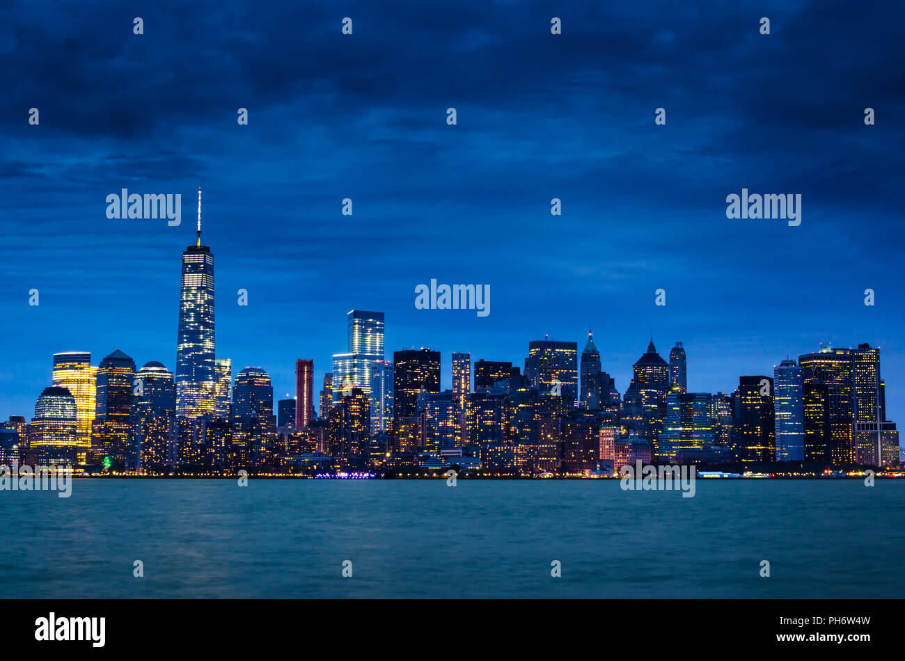 New York City Downtown bei Nacht. Manhattan Skyline bei Nacht mit beleuchteten Wolkenkratzer und bewölkter Himmel das Foto von Ellis Island. Stockfoto