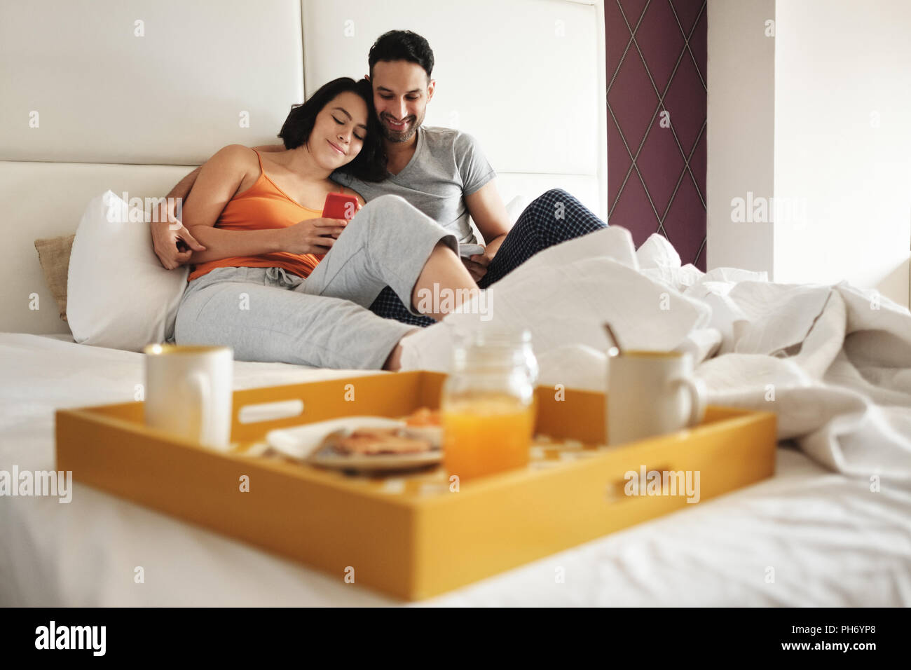 Der Mann und die Frau beim Frühstück im Bett mit Phone Stockfoto