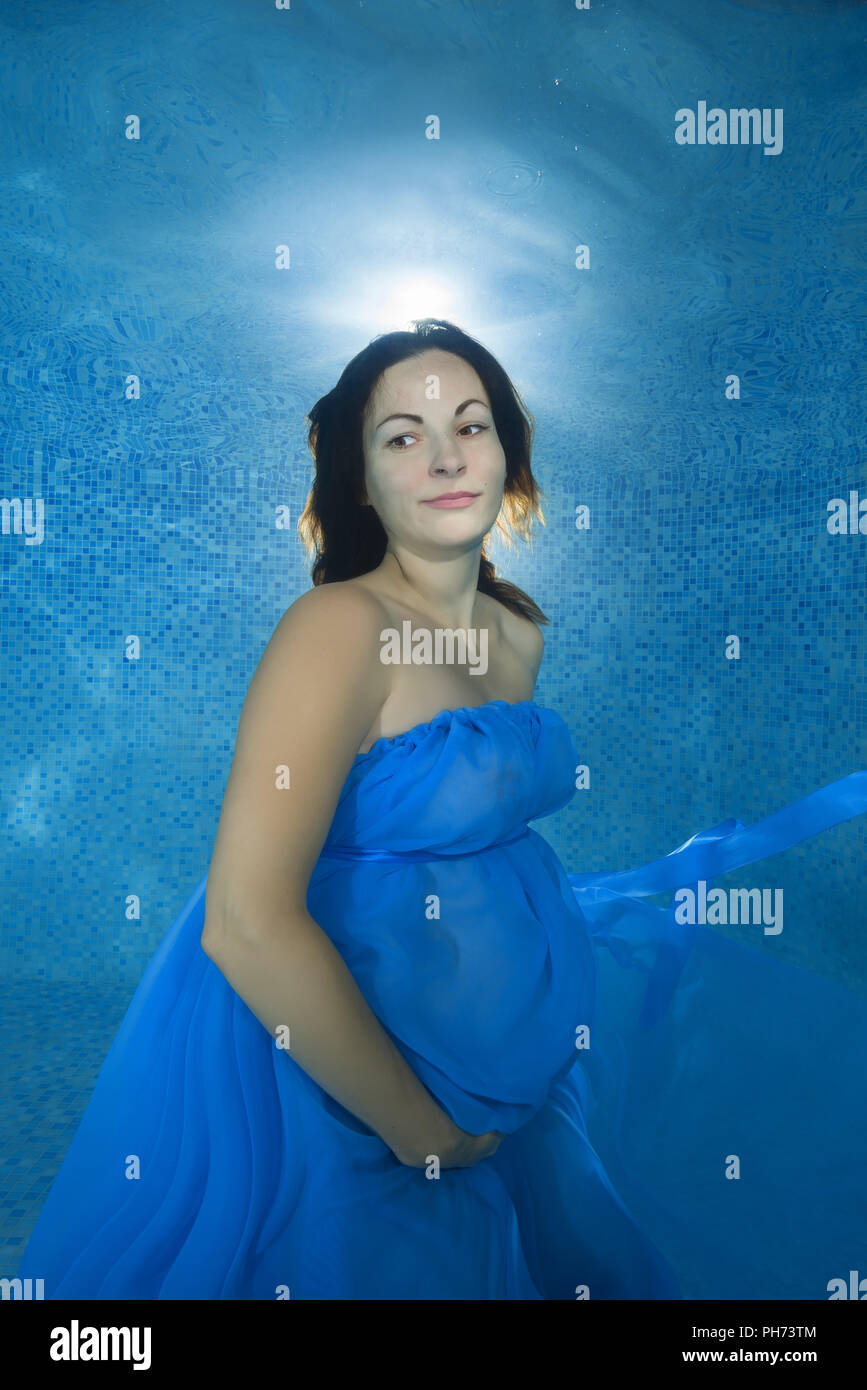 Schwangere Frau in einem blauen Kleid unter Wasser im Pool posiert Stockfoto