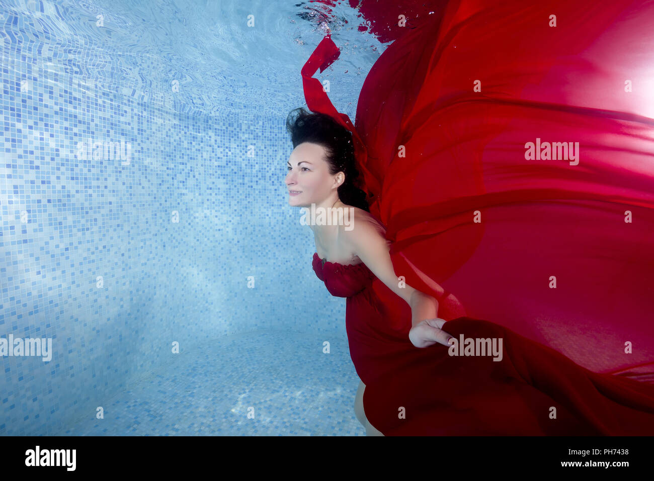 Schwangere Frau im roten Kleid unter Wasser im Pool posiert Stockfoto