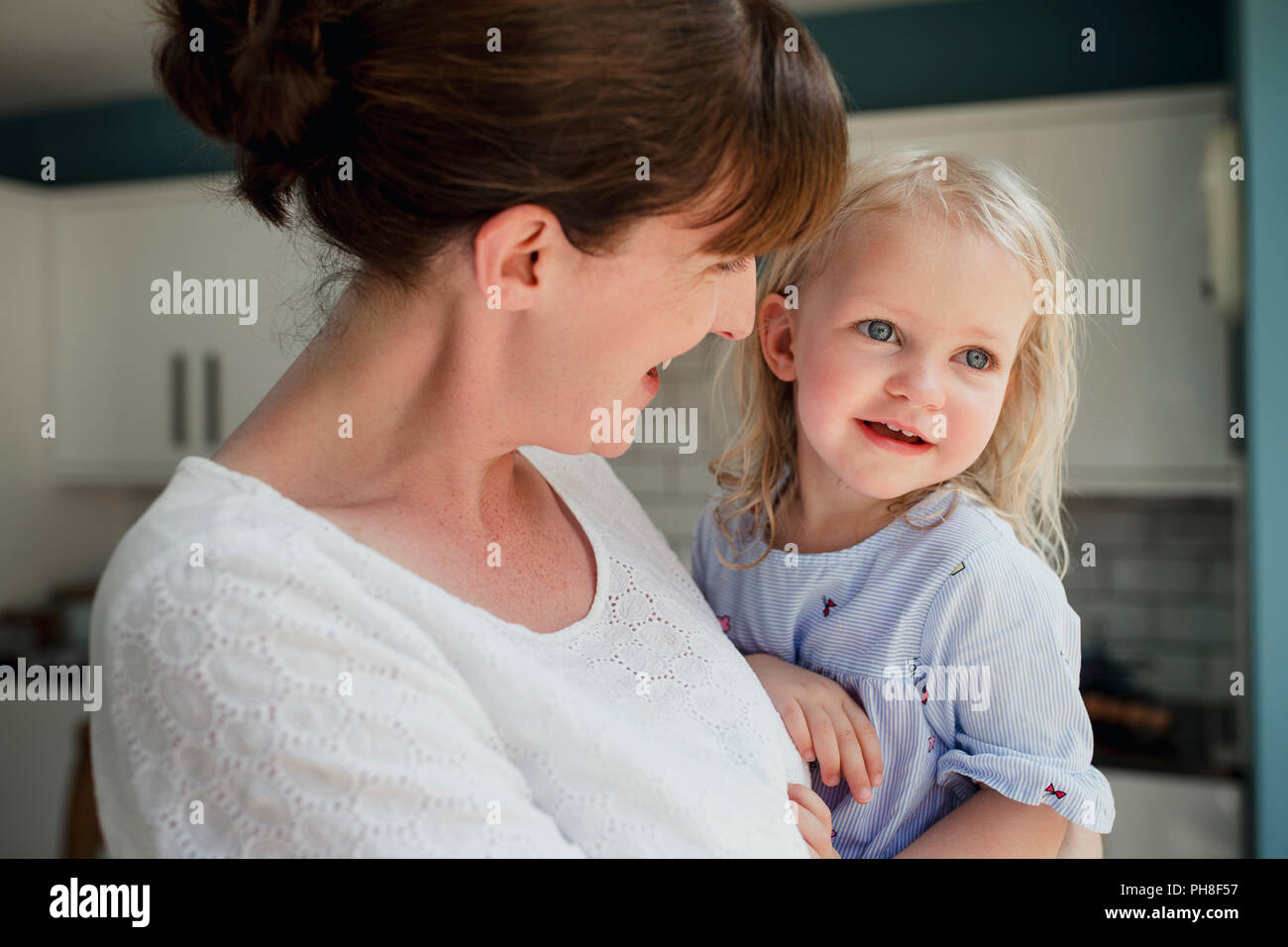 Seitenansicht einer Mutter sprechen und ein Lächeln auf Ihre Tochter, die auch lächelt. Mitte der erwachsenen Mutter hielt ihre Tochter und der Fürsorge für ihre. Stockfoto