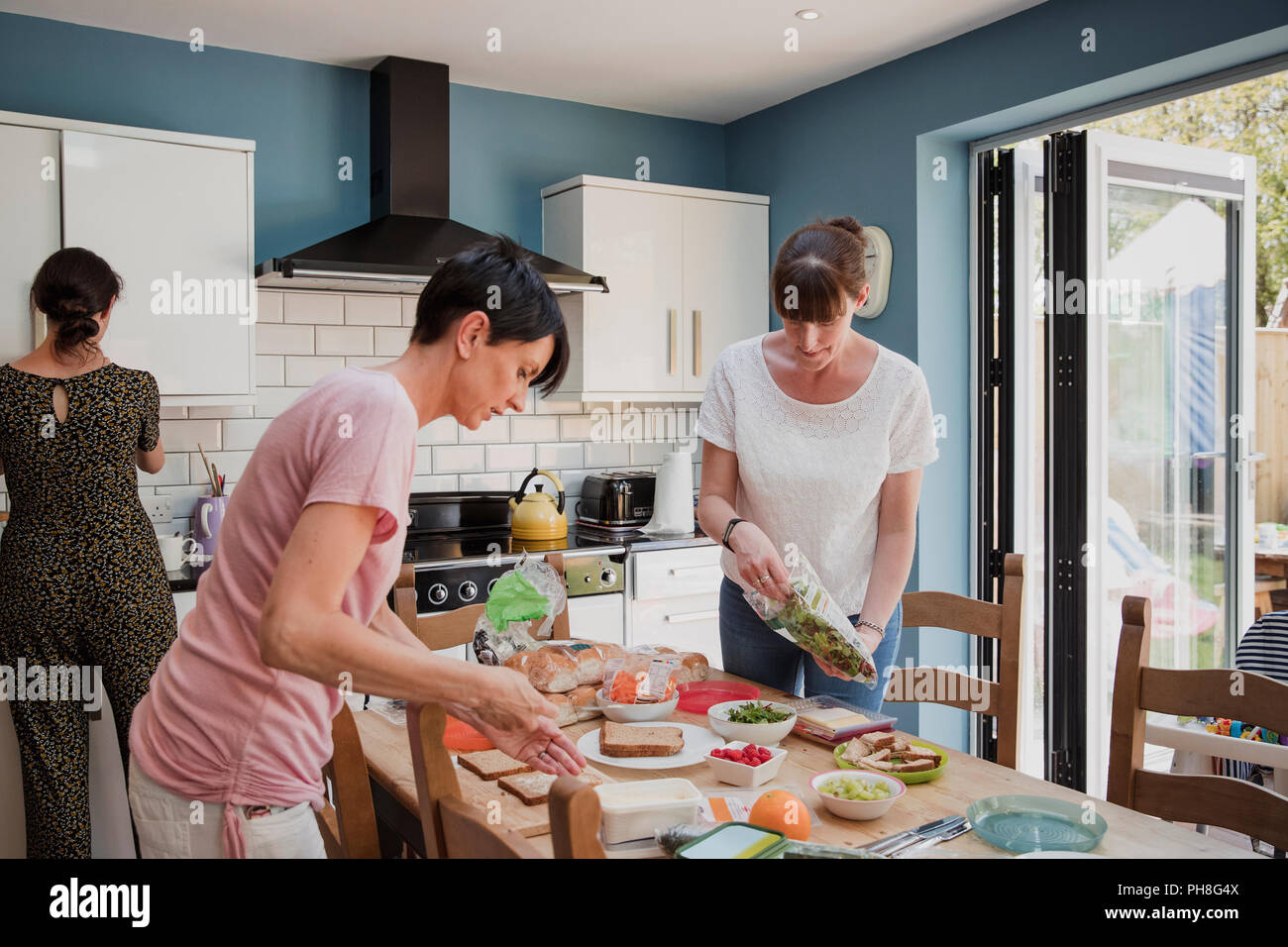 Thre Mitte der erwachsenen Frauen stehen in der Küche ein Esstisch. Die Frauen ae Vorbereitung der Speisen zum Mittagessen. Preping einige Salate und Sandwiches. Stockfoto