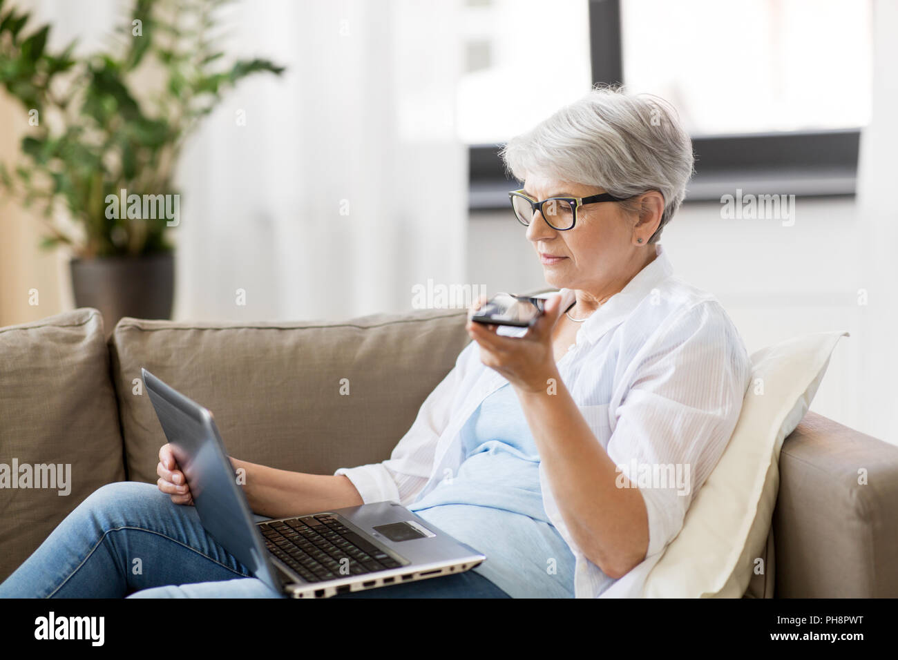 Alte Frau mit Laptop Datensätze Stimme von Smartphone Stockfoto