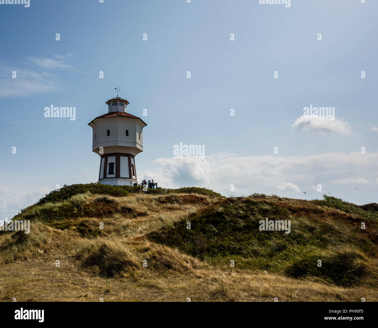 Wasserturm Langeoog. Deutschland, Deutschland. Ein Weg zu einer touristischen Attraktion führt, die ikonische White Water Tower - Wasserturm. Das Gras auf den Sanddünen haben von der Sonne gebleicht während der Hitzewelle dieses Sommers. Das Foto ist zurück - leuchtet ein Licht blauer Himmel und tiefe Schatten auf den Betrachter zu werfen Stockfoto