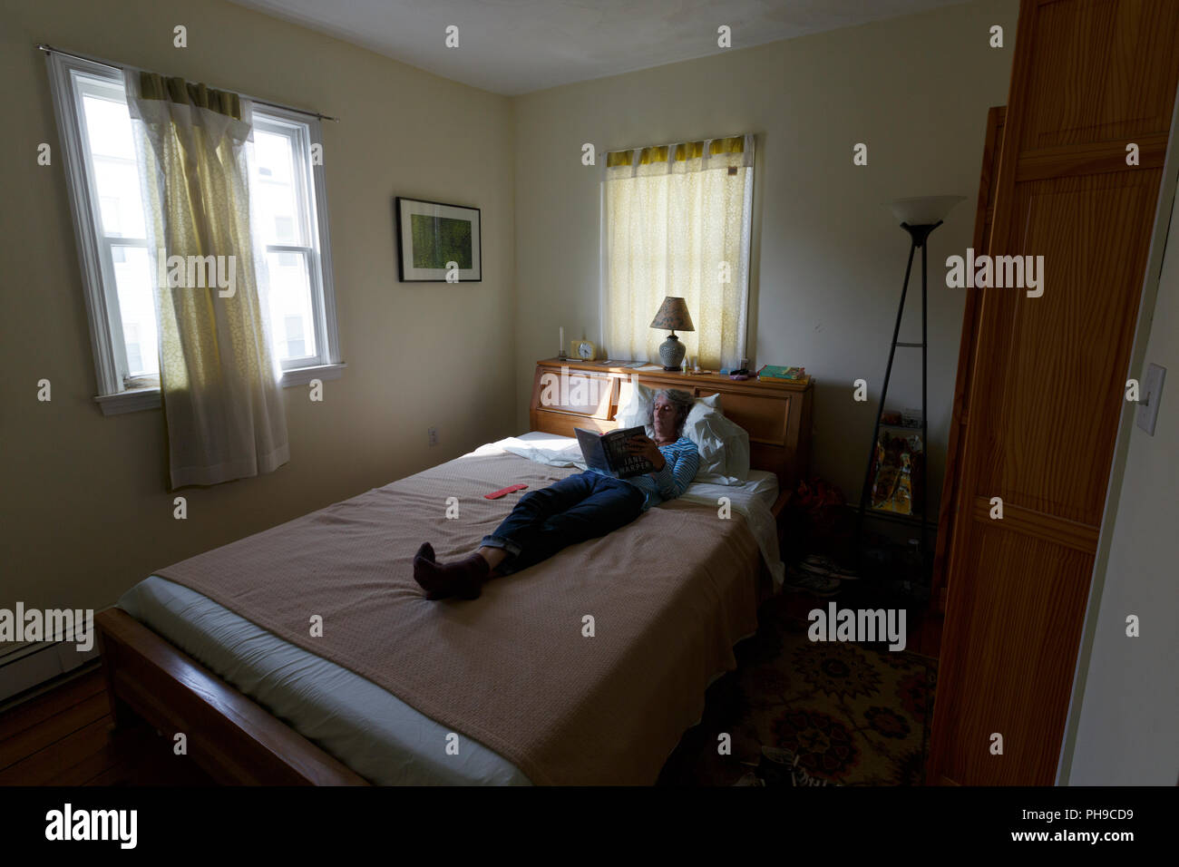Frau Lesen im Bett; am späten Nachmittag diffuses Licht Boston Massachusetts USA Stockfoto