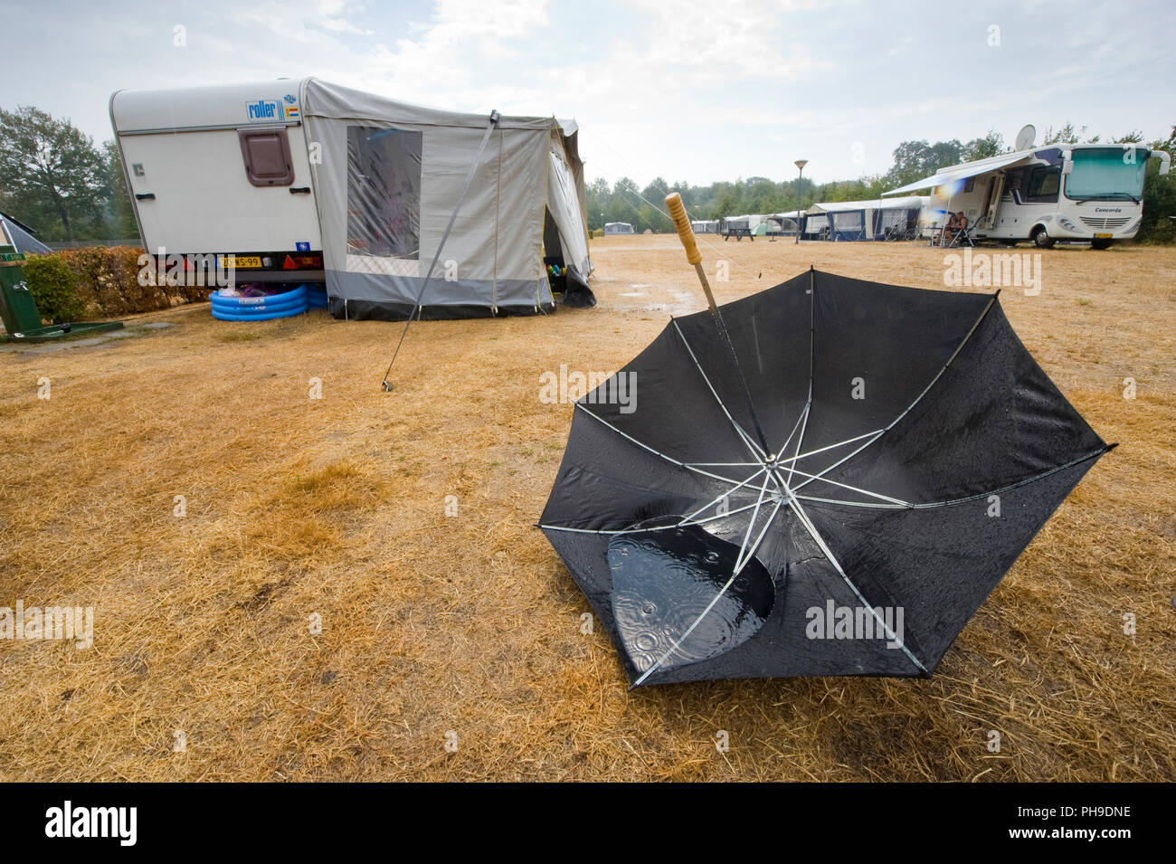 HAAKSBERGEN, Niederlande - 09.August 2018: Ein Regenschirm ist auf dem Kopf liegend auf dem Boden nach einem Regenguss auf einem niederländischen Camping im Sommer. Stockfoto