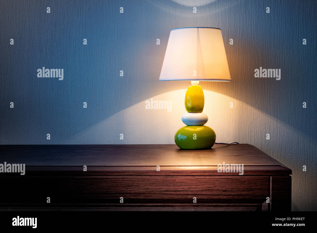 Kleine gelbe, graue und grüne Lampe auf Holz Kommode oder ein Nachttisch, beleuchten die Wand mit Tapeten in der Nacht oder am späten Abend abgedeckt. Weich Stockfoto