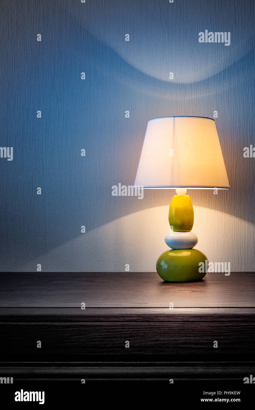 Kleine gelbe, graue und grüne Lampe auf Holz Kommode oder ein Nachttisch, beleuchten die Wand mit Tapeten in der Nacht oder am späten Abend abgedeckt. Weich Stockfoto