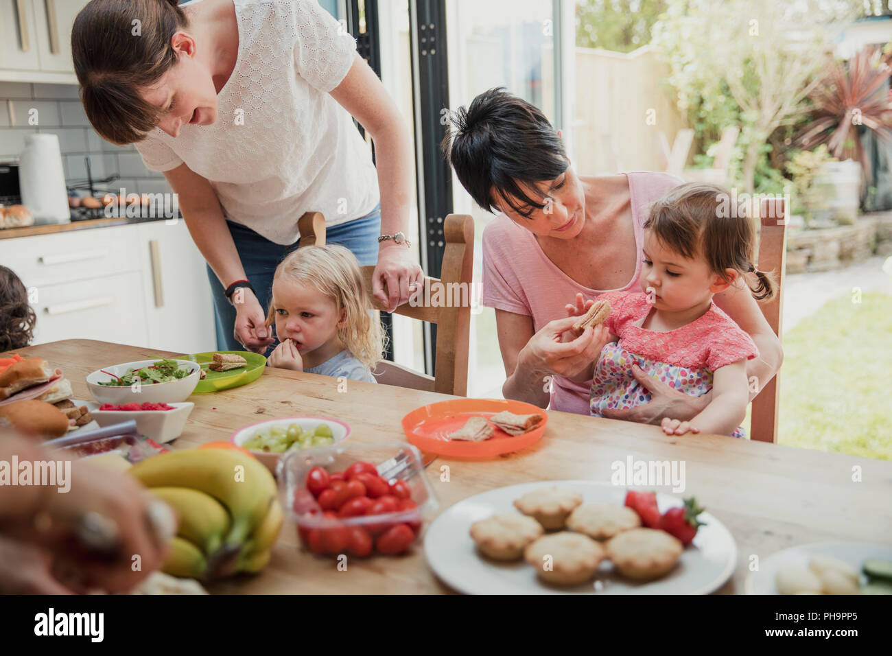 Zwei mittig nach Mütter ihre Töchter neue Speisen zu probieren. Sie sind in der Küche genießen Ihre gesundes Mittagessen. Stockfoto