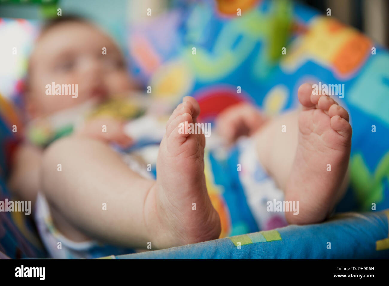 Nicht erkennbare Baby entspannen in einem Baby Bouncer. Fokus auf den Vordergrund auf der Babys Füße. Der Hintergrund des Bildes ist unscharf. Stockfoto
