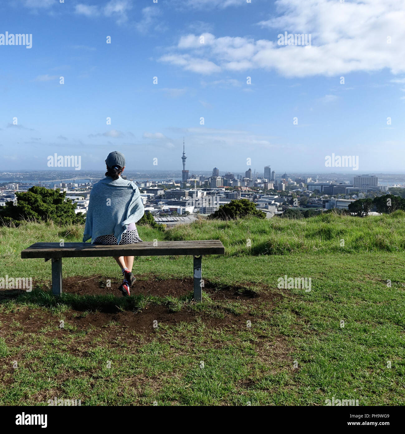 Frau sitzt auf der Bank wird mit Blick auf die Skyline von Auckland Stockfoto