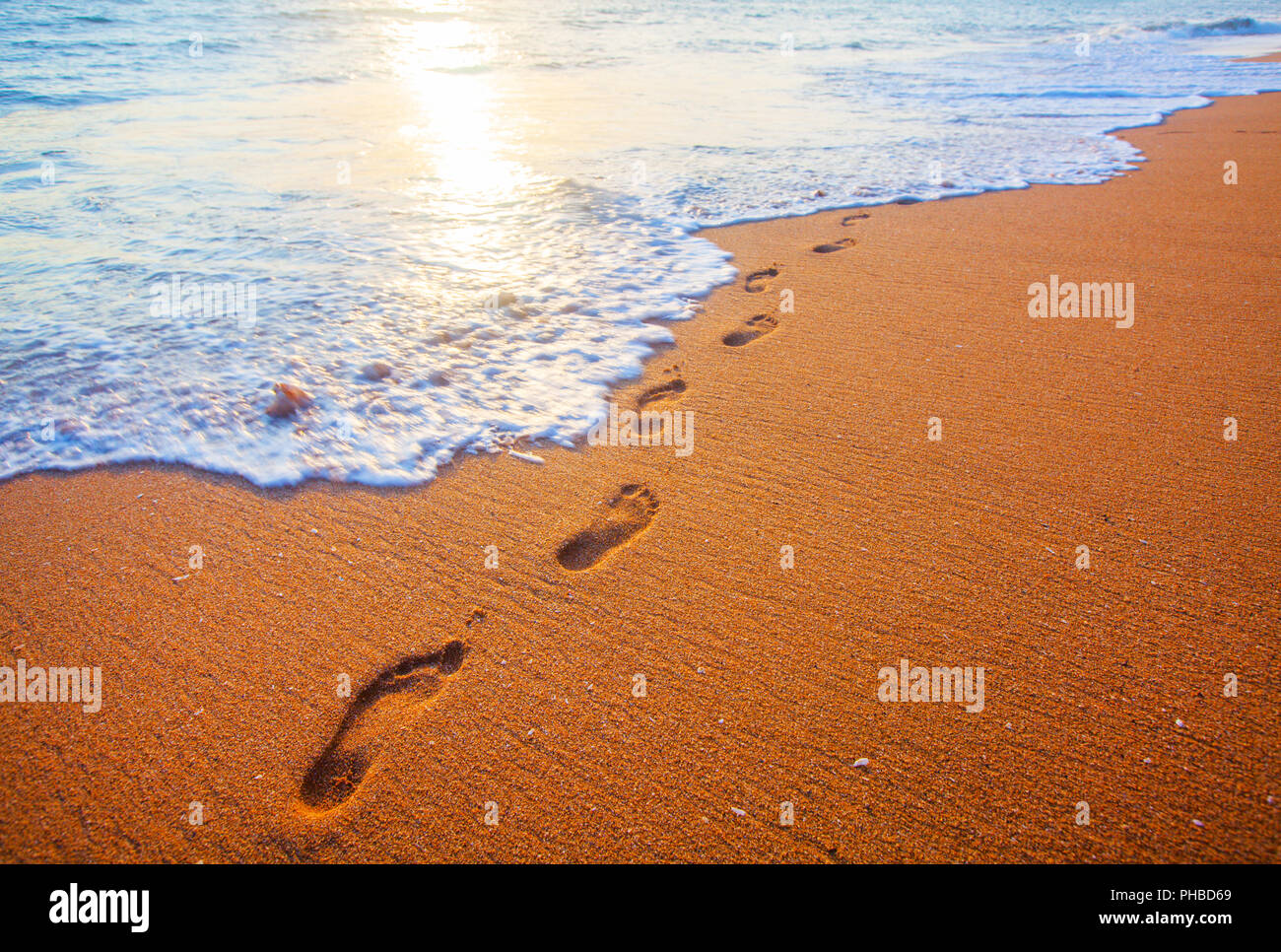 Strand, Wellen und Fußabdrücke bei Sonnenuntergang Stockfoto