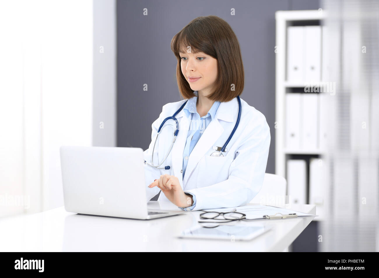 Arzt tippt auf Laptop beim Sitzen am weißen Tisch im Krankenhaus. Arzt bei der Arbeit. Medizin und Gesundheit Konzept. Stockfoto