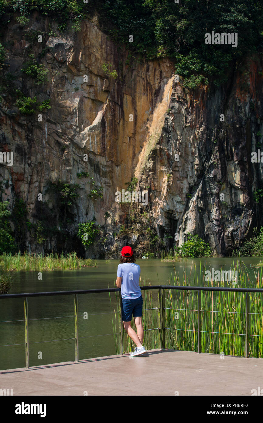 Vertikal. Rückansicht einer Frau, die aus dem Steinbruch blickt. Suchen Sie in einem Steinbruchpark nach Balance und verbinden Sie sich mit der Natur. Singapur. Stockfoto