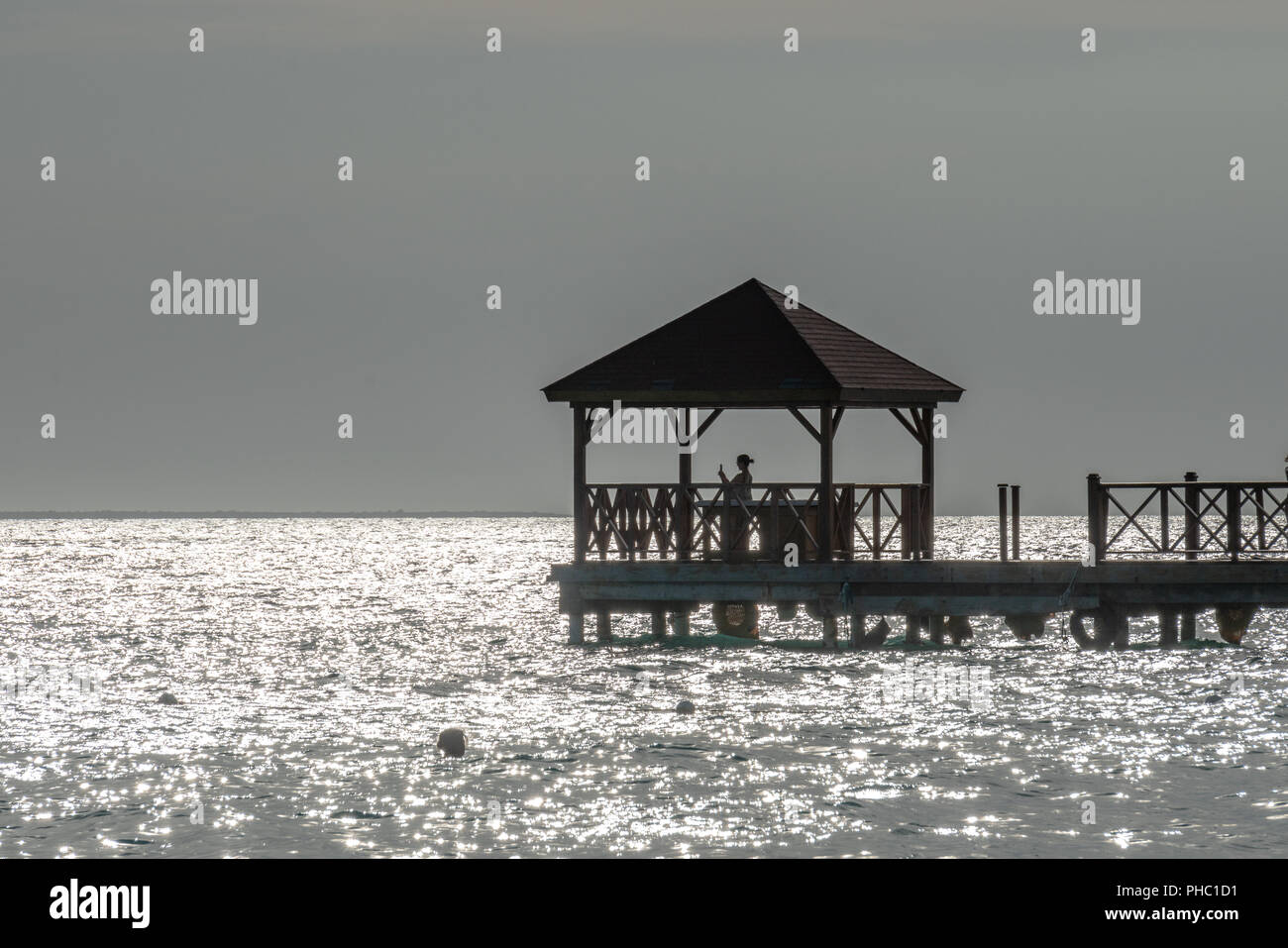 Bayahibe, Dominikanische Republik, 27. August 2018. Eine touristische verwendet Ihr Telefon an einer Pier über das Karibische Meer. Die grauen Look ist aufgrund der extremen Hintergrundbeleuchtung Stockfoto