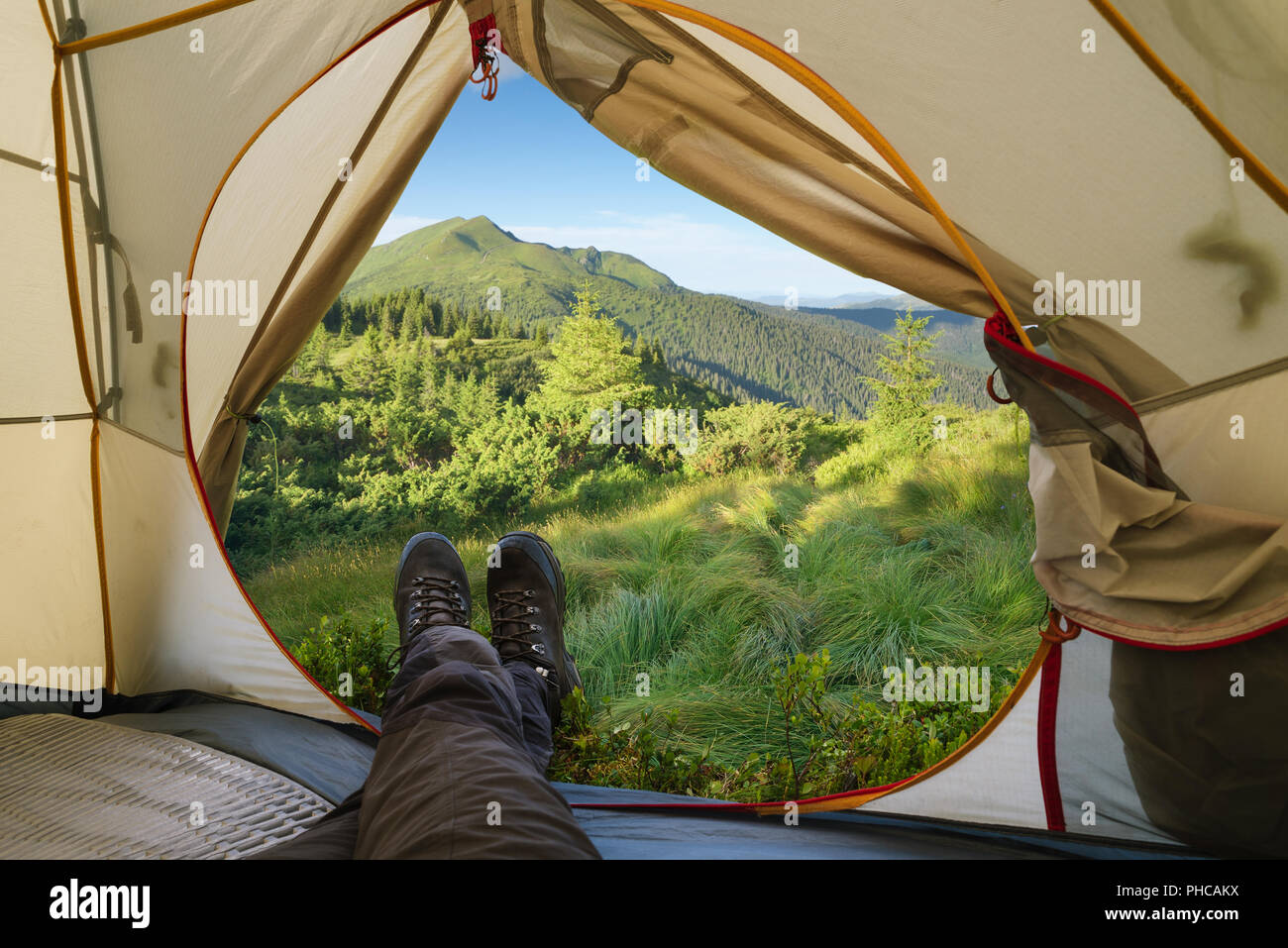 Camping in den Bergen. Sommer Wandern. Blick aus einem touristischen Zelt auf einem Höhepunkt. Kerl in Trekkingschuhe. Stockfoto