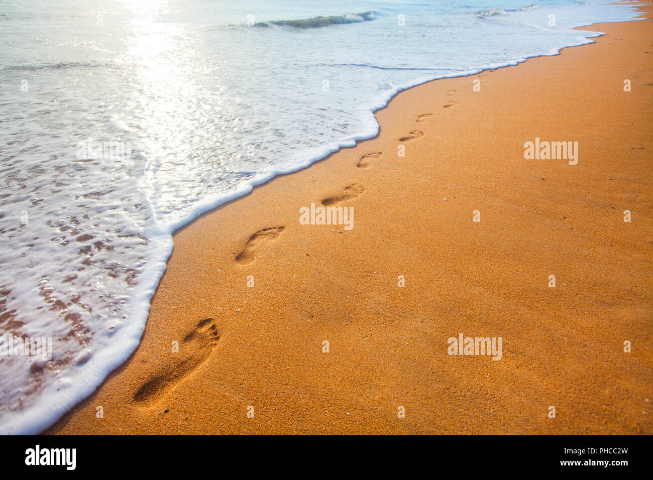 Strand, Wellen und Fußabdrücke bei Sonnenuntergang Stockfoto