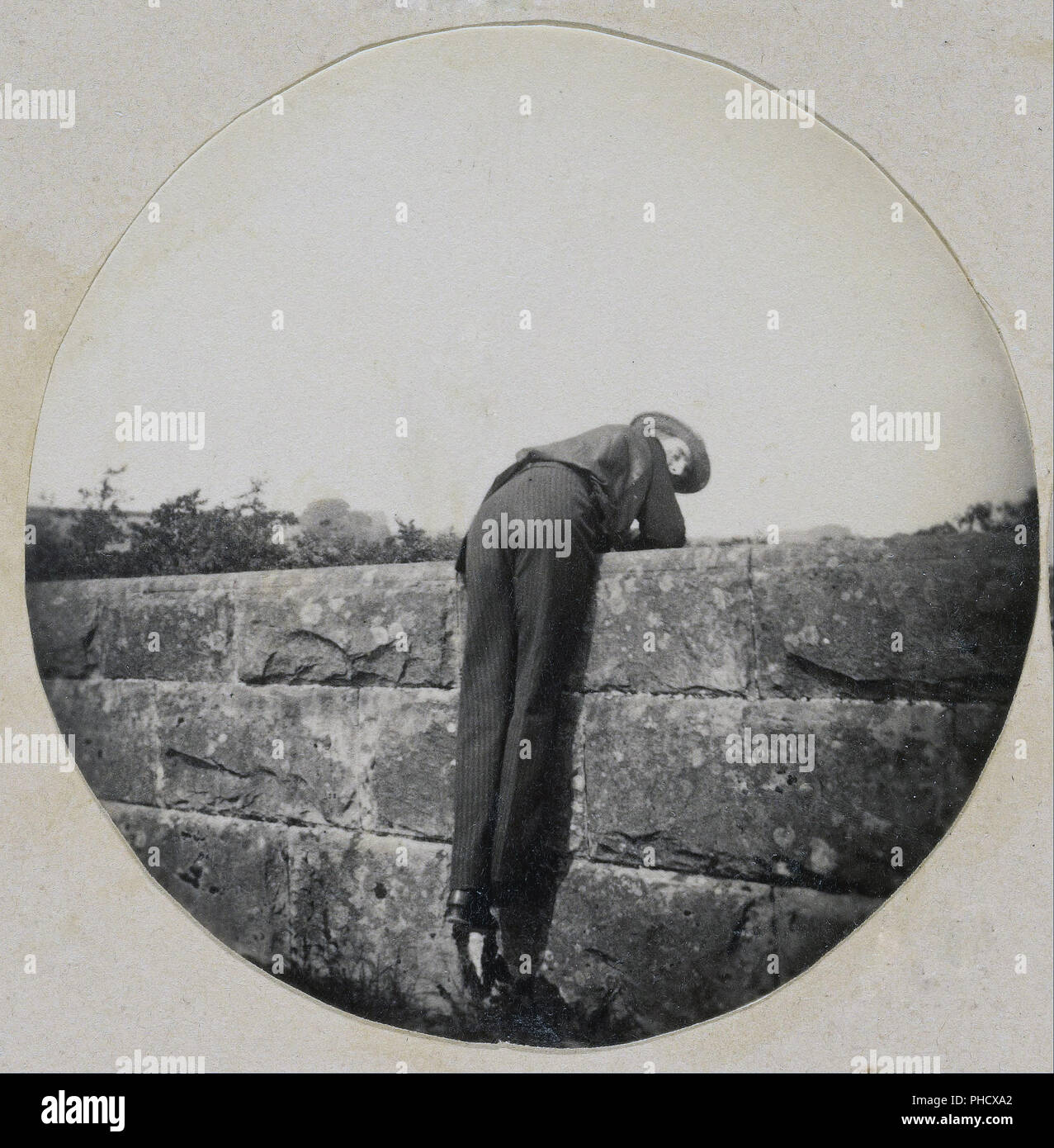 Mann in Hut beugte sich über eine Mauer aus Stein Stockfoto