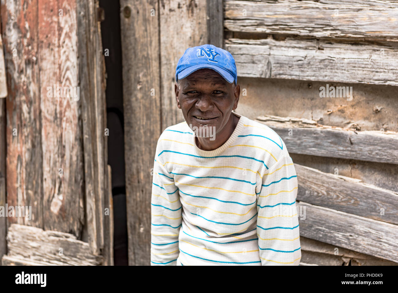 Portrait eines älteren Afro Mann gegen eine reich strukturierte Hintergrund einer weatherbeaten Holzhaus. Er zeigt seine Unterstützung für die NY Yankees. Stockfoto