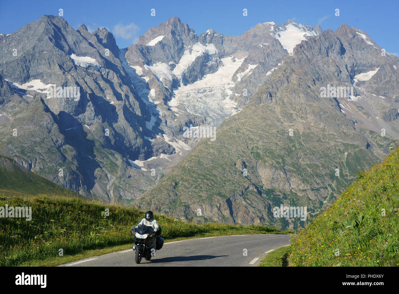 Motorradfahrer, die mit den hohen Gipfeln und Gletschern des Écrins-Massivs im Hintergrund fahren. Zwischen Col du Lautaret und Col du Galibier, Frankreich. Stockfoto