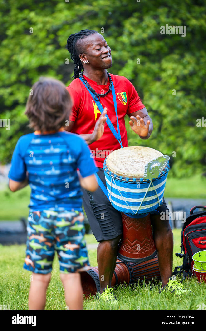 African American männlichen Schlagzeuger spielen seiner djembe Bongo vor einem Kind, der ihn beobachtete. Stockfoto