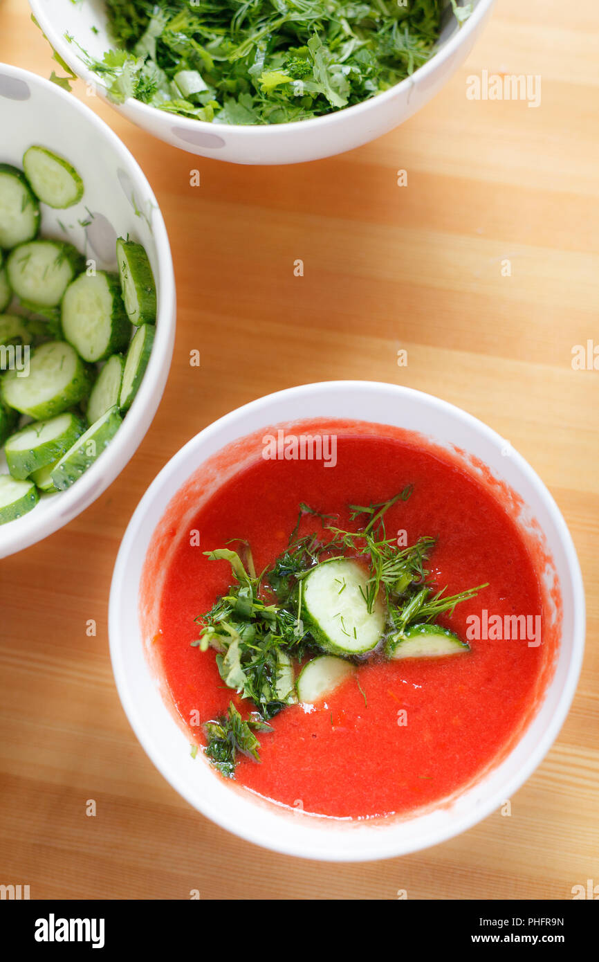 Leckere Tomatensuppe mit aromatischen Gewürzen und organischen Gurken in einer weißen Schüssel auf einen hölzernen Tisch. Gesundes Mittagessen. Hausgemachte Speisen. Stockfoto