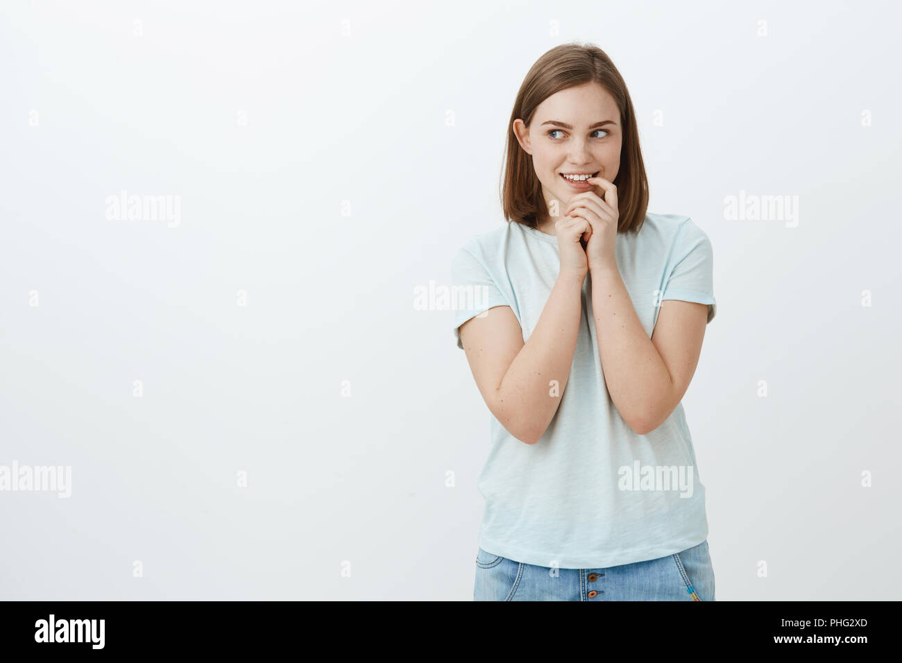 Kreative geheimnisvolle wunderschöne junge Frau mit braunem Haar und großen Ohr halten den Finger auf die Unterlippe lächelnd und anstarrt, als ob, interessante Idee oder Wunsch stehend über grauer Hintergrund links Stockfoto