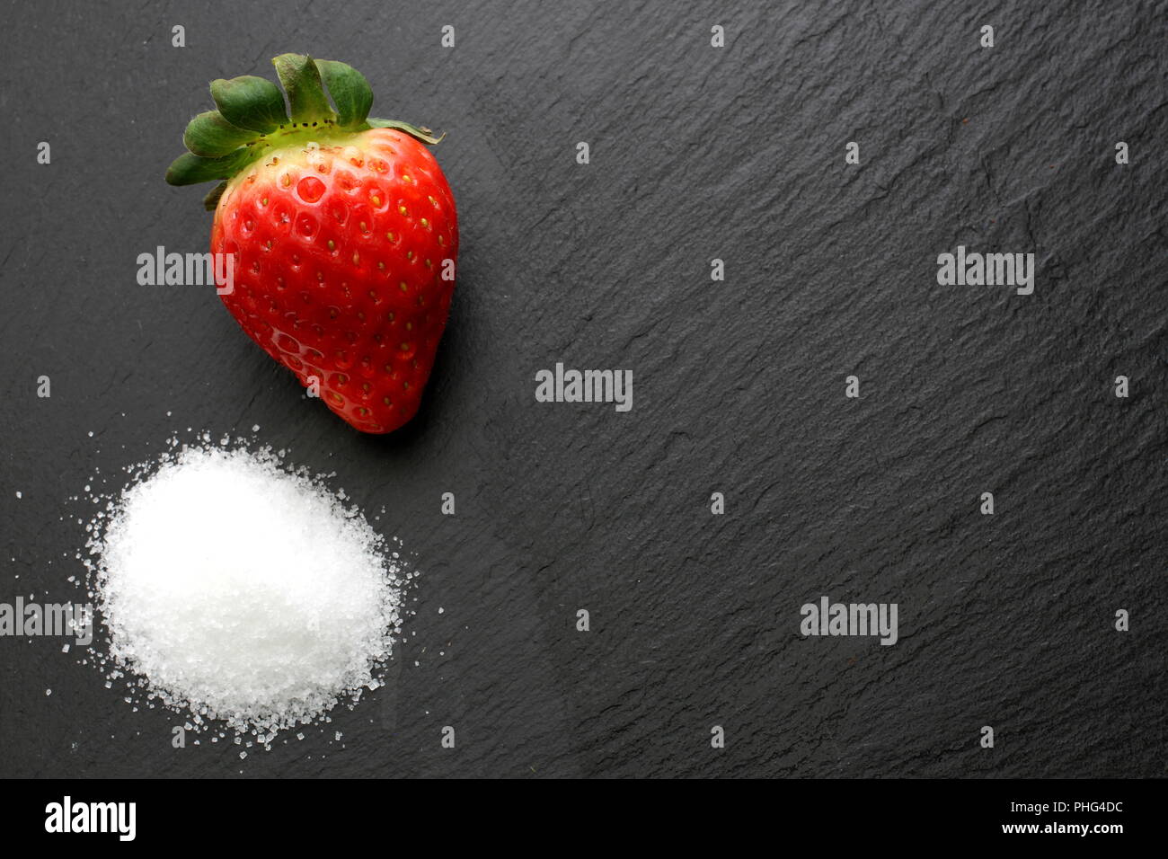 Single reife Erdbeeren mit Kristallzucker auf schiefer Platte Stockfoto