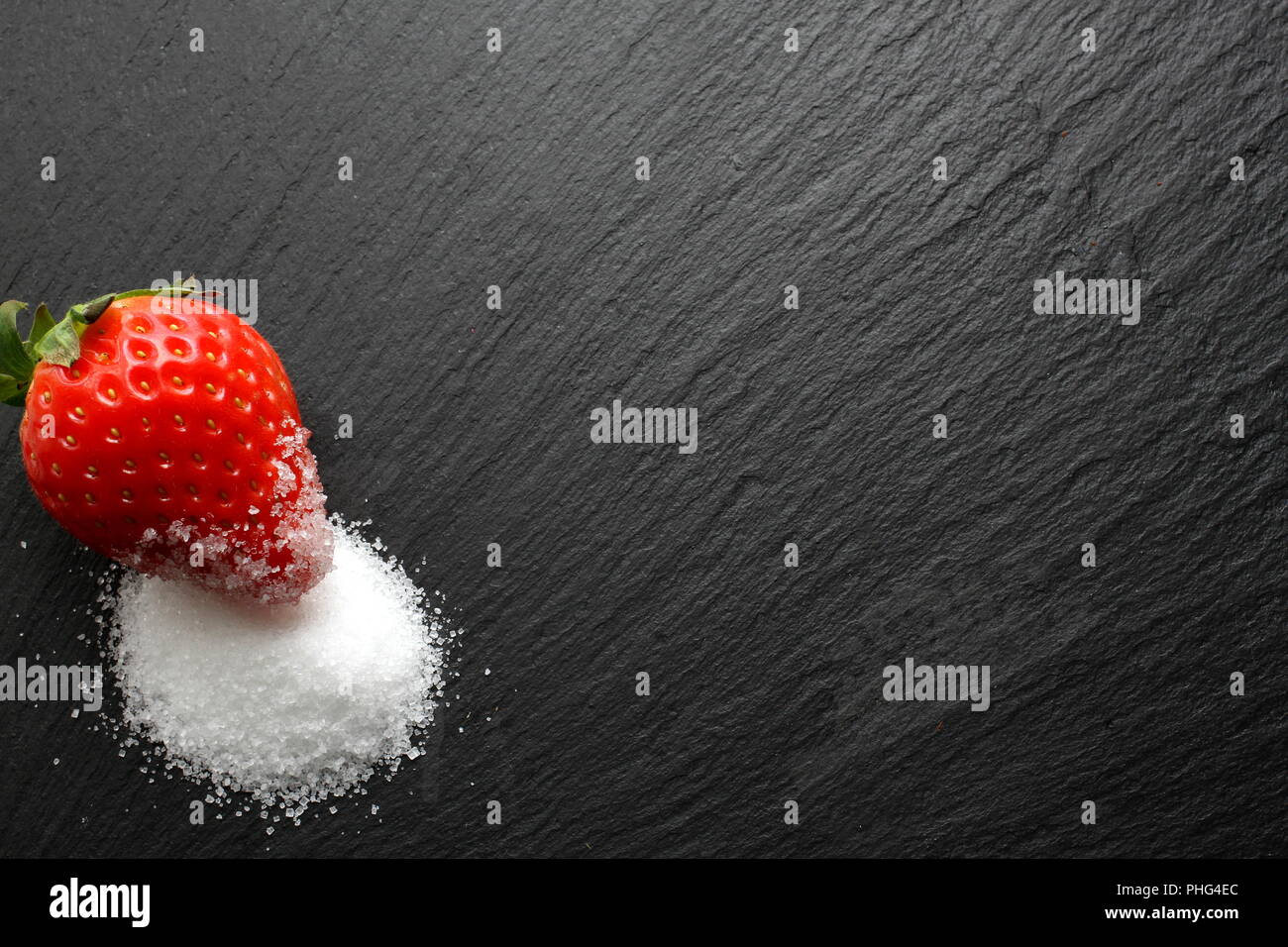 Single reife Erdbeeren mit Kristallzucker auf schiefer Platte Stockfoto
