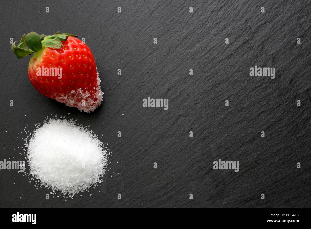 Single reife Erdbeeren mit Kristallzucker auf schiefer Platte Stockfoto
