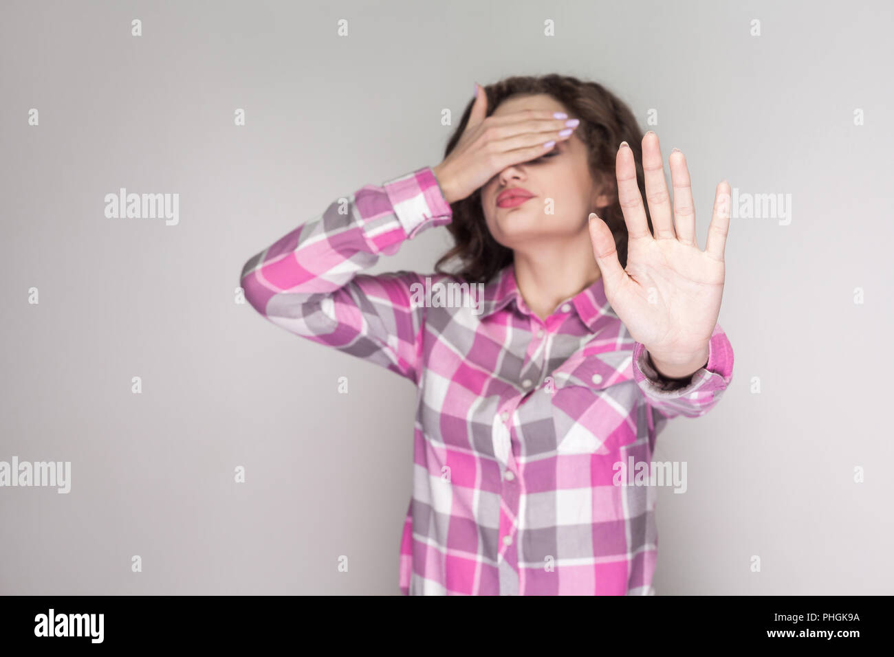 Ich sehe es nicht sehen wollen. verwirrt Mädchen mit rosa kariertem Hemd und Angst und schloss ihre Augen mit der Hand und versuchen zu blockieren. indoor Studi Stockfoto