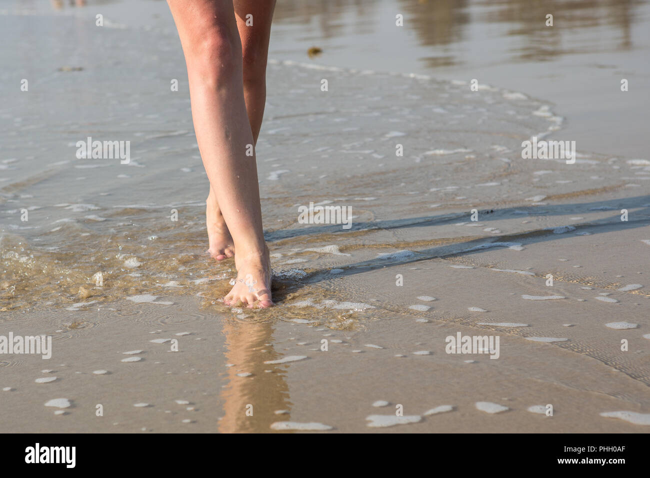 Eine Frau, die zu Fuß am Strand entlang an einem sonnigen Tag Stockfoto