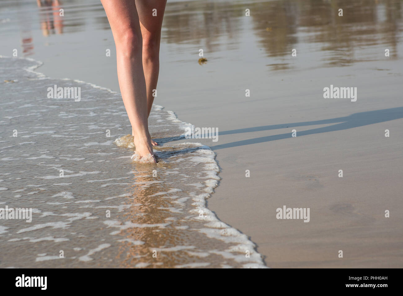 Eine Frau, die zu Fuß am Strand entlang an einem sonnigen Tag Stockfoto
