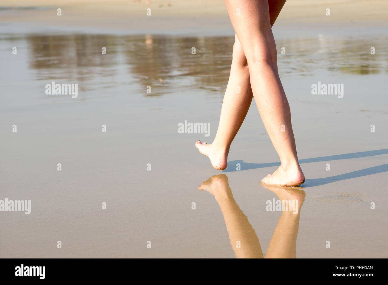 Eine Frau, die zu Fuß am Strand entlang an einem sonnigen Tag Stockfoto