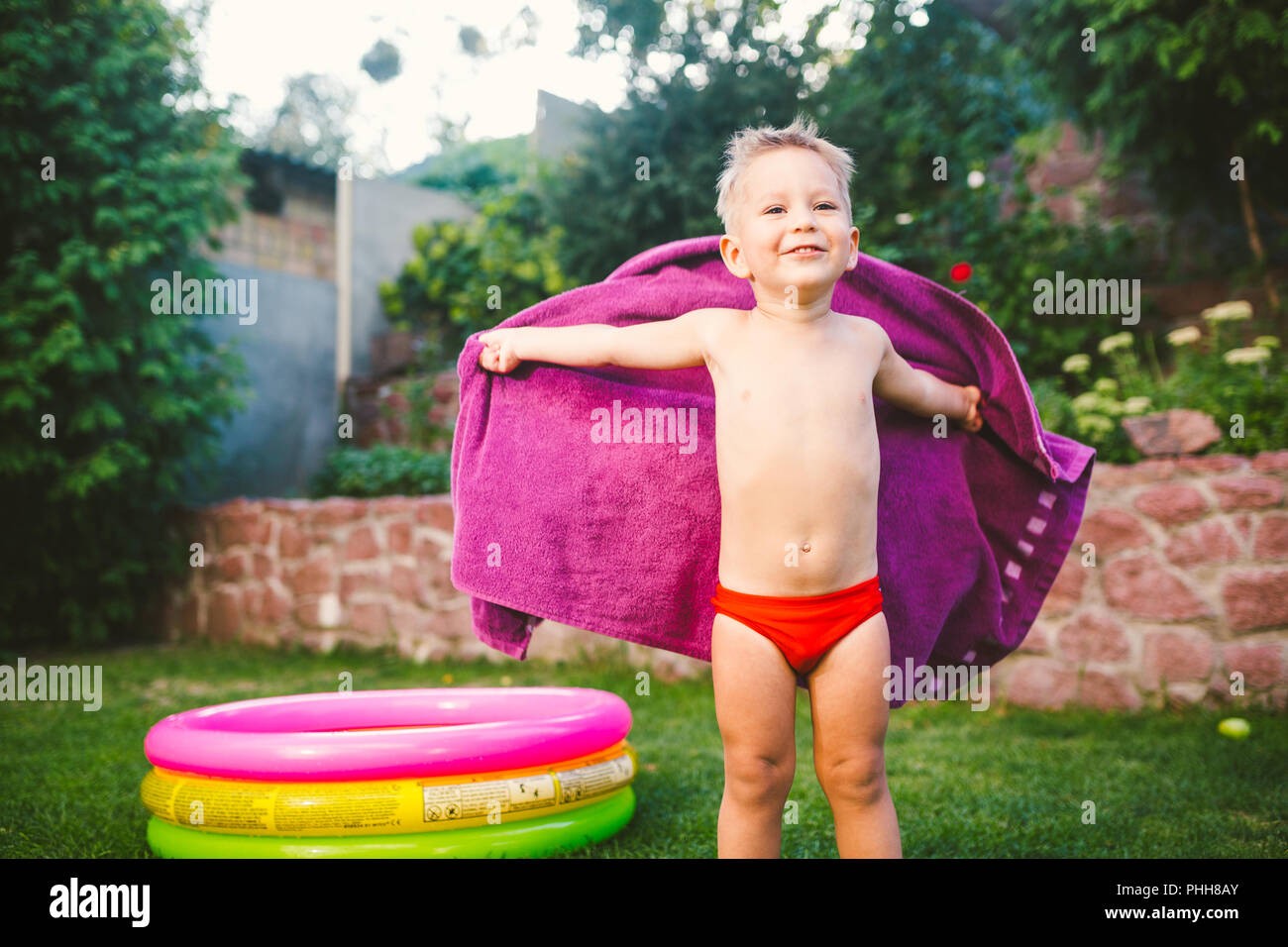Sommer Urlaub Thema. Eine kleine 3 jährige Kaukasier Junge spielt im Hinterhof eines Hauses auf dem Gras in der Nähe von eine Runde aufblasbare farbige Pool u gewickelt Stockfoto