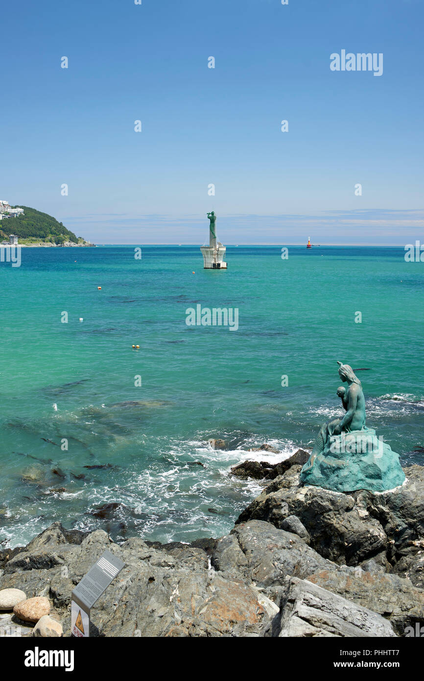Haeundae Bay, Busan, Korea. Legende der Prinzessin Hwangok und die Meerjungfrau von Dongbaek Insel - bronzestatue an der felsigen Küste. Leuchtturm Stockfoto