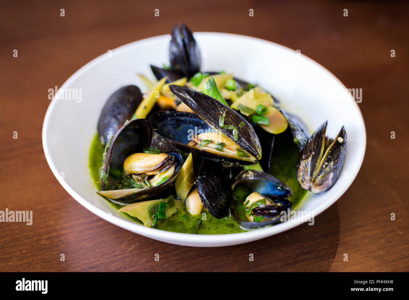 Muscheln in Schalen in einer weißen Schüssel mit grüner Soße auf einen Esstisch. Stockfoto