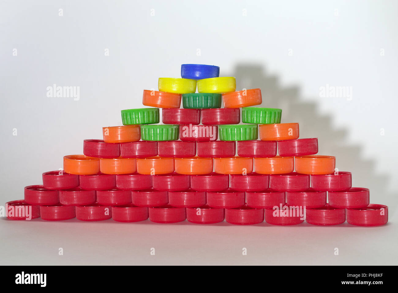 Flache Pyramiden aus farbigem Kunststoff Flaschenverschlüsse wirft Schatten in Form von Treppen auf grauem Hintergrund Stockfoto