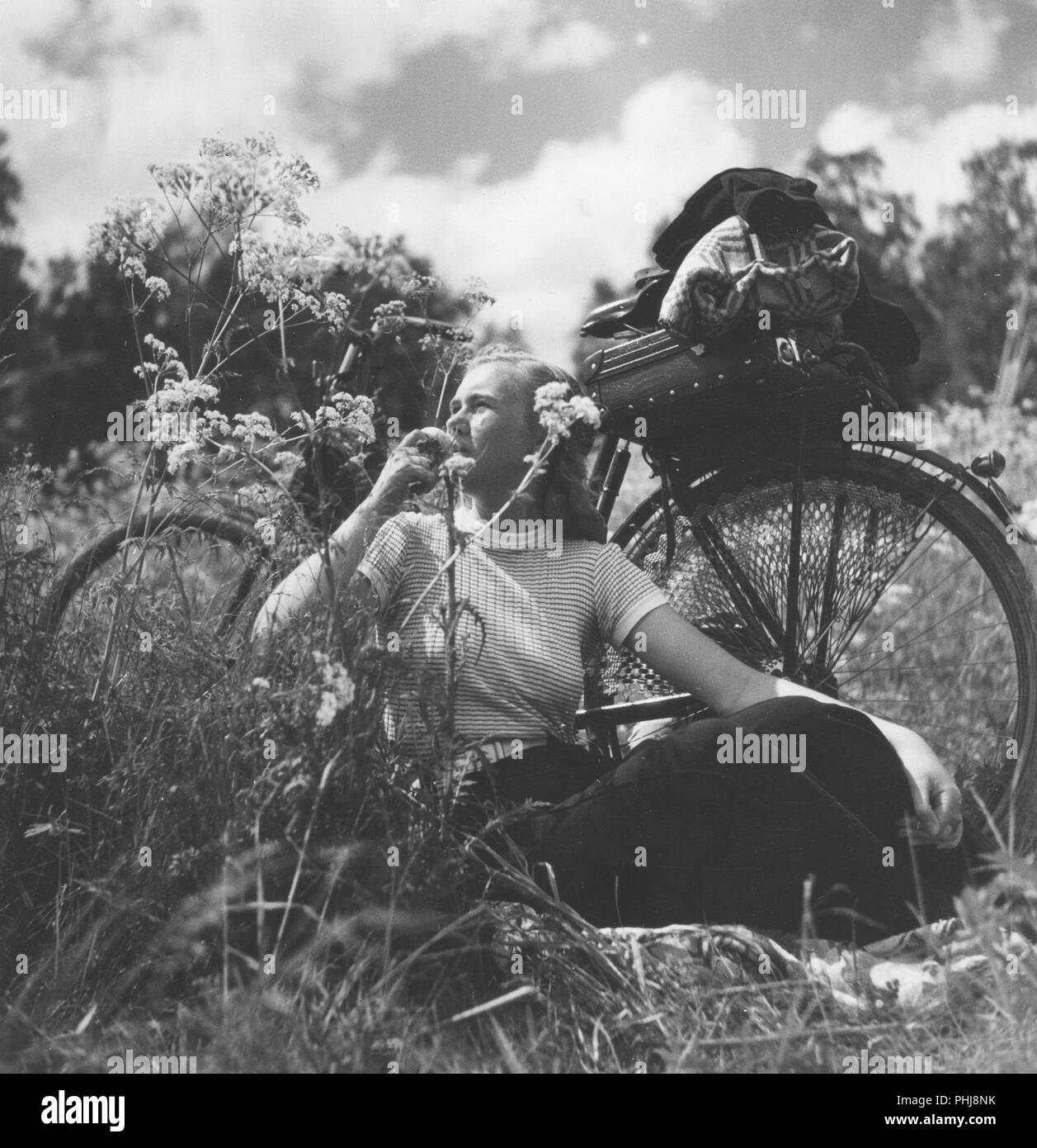 1940 Frau auf einem Fahrrad. Eine junge Frau hat ihr Fahrrad genommen und sich erholend auf einer Wiese. Schweden 1946 Stockfoto