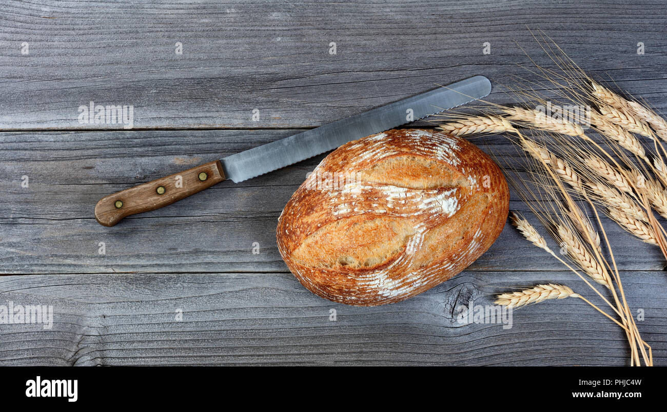 Ansicht von oben von gebackenen ganzen Laib Brot mit Messer und Weizen Stiele auf rustikalen hölzernen Brettern Stockfoto