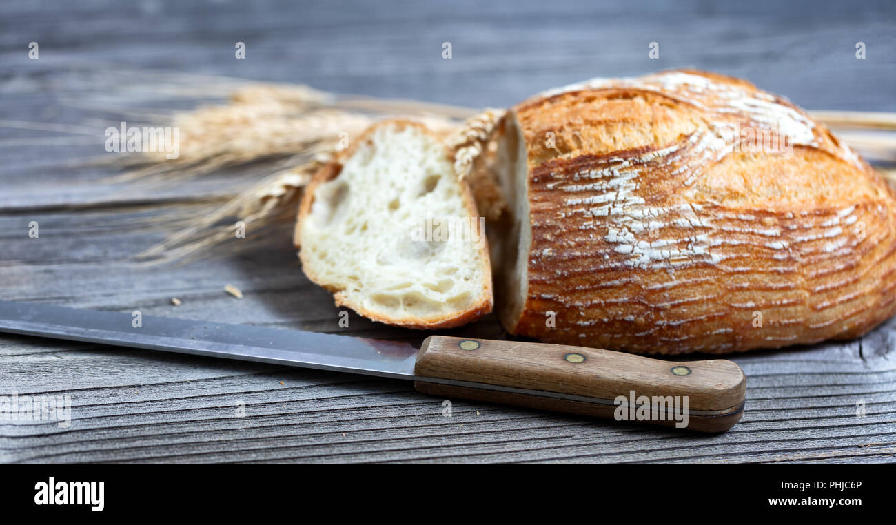 Nahaufnahme einer in Scheiben geschnittenen gebackene ganze Laib Brot mit Messer und Weizen Stiele auf rustikalen hölzernen Brettern Stockfoto