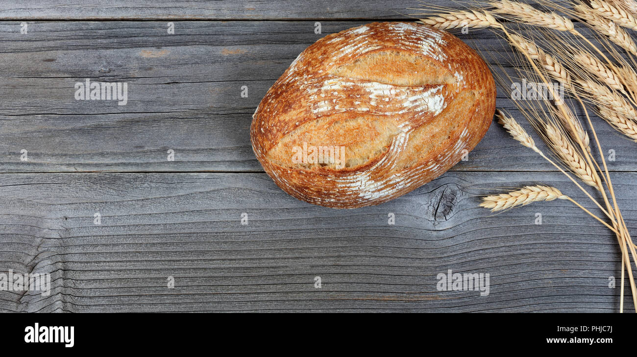 Ansicht des ganzen Laib Brot gebacken und Weizen Stiele auf rustikalen hölzernen Brettern Stockfoto
