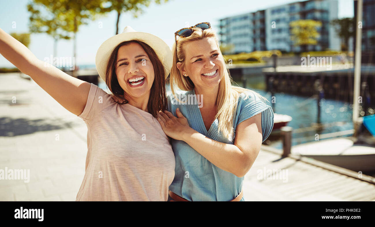 Zwei lachende Junge weibliche Freunde, eine gute Zeit zu Fuß Arm in Arm zusammen in der Stadt im Sommer Stockfoto