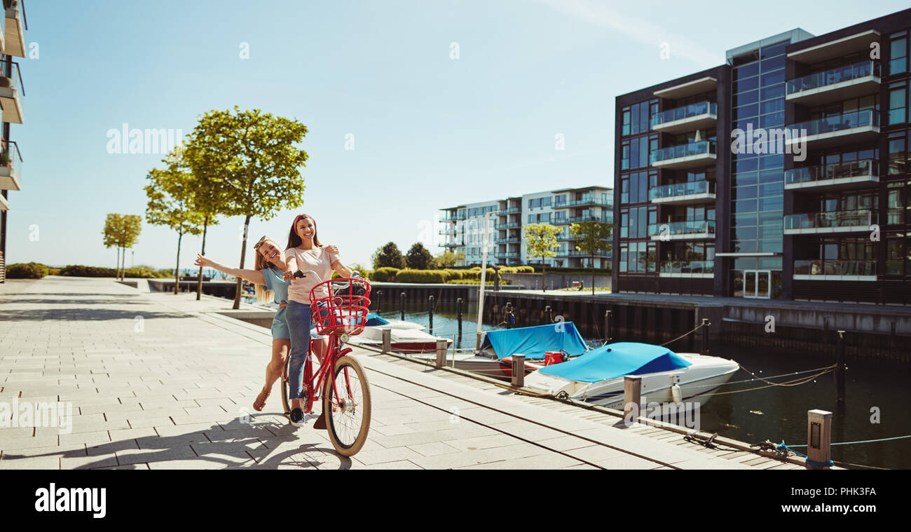 Zwei unbeschwerte Junge weibliche Freunde Reiten auf einem Fahrrad durch die Stadt an einem sonnigen Sommertag Stockfoto