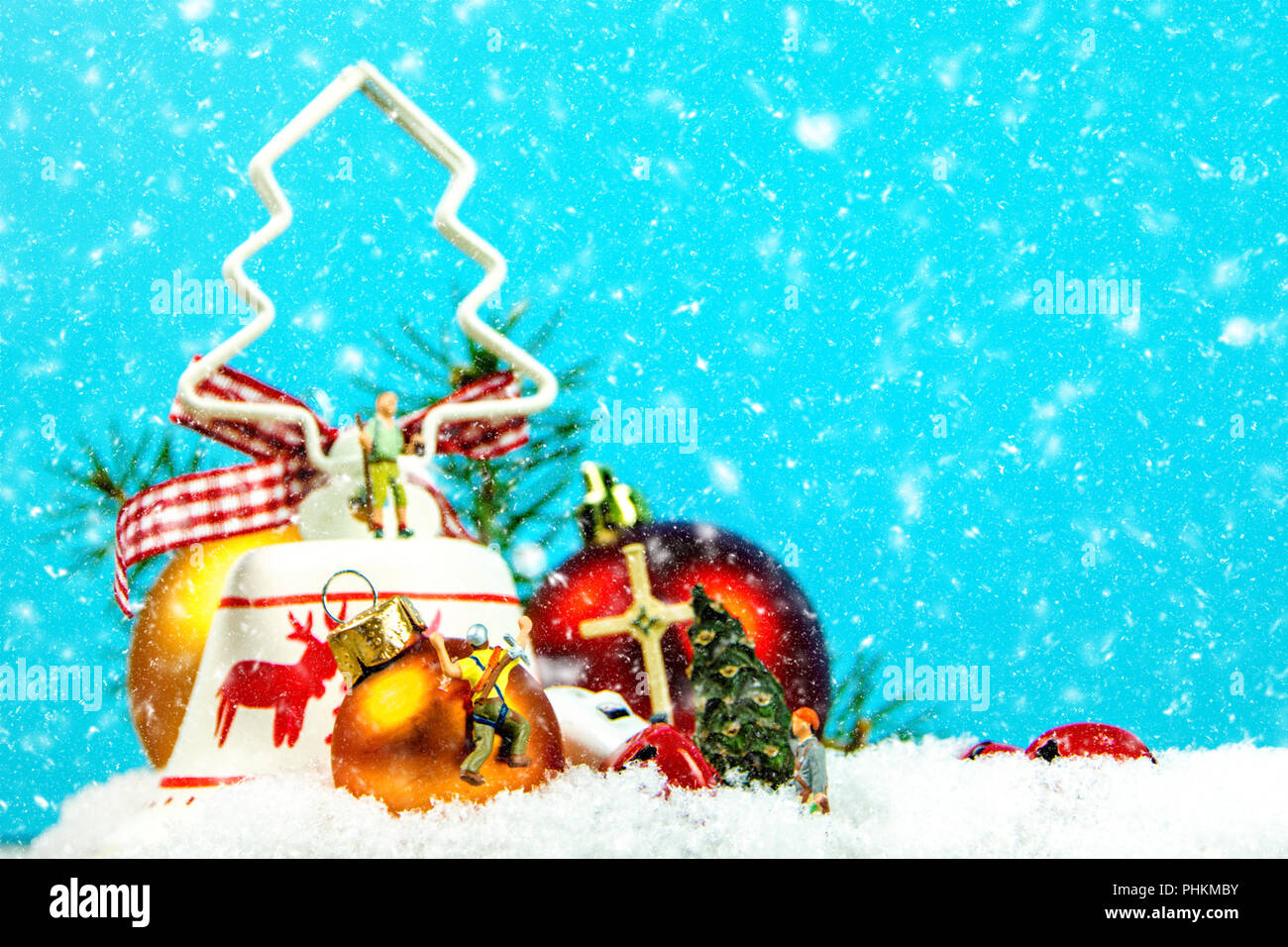 Nahaufnahme der Weihnachtsdekoration mit Miniatur Figuren und Schneefall in den blauen Hintergrund mit Jingle Bells, Nadeln und bunte Weihnachten bal Stockfoto