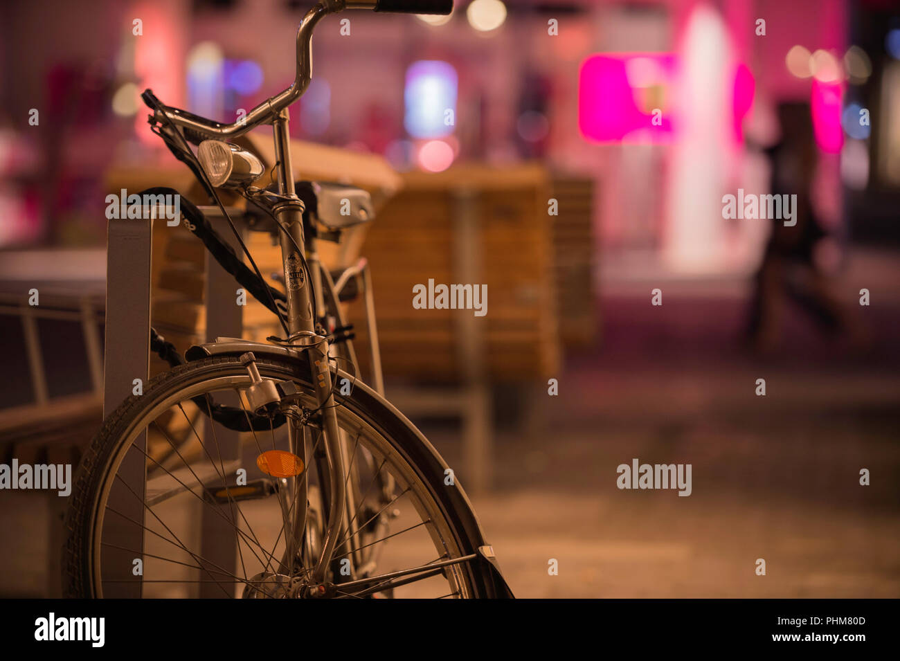 Eine alte fahioned Fahrrad eine Straße Sitzbank bei Nacht mit bunten Lichtern im Hintergrund gesperrt. Stockfoto