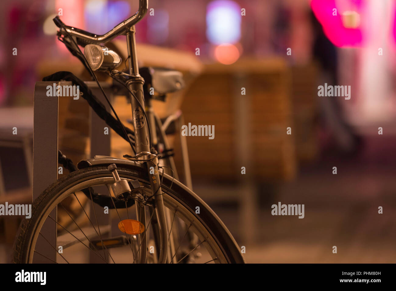 Eine alte fahioned Fahrrad eine Straße Sitzbank bei Nacht mit bunten Lichtern im Hintergrund gesperrt. Stockfoto