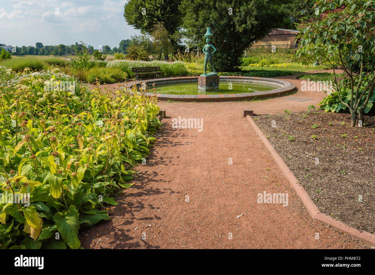 Blick auf die Statue, Bäumen und Blumen an einem Weg am Rheinpark Golzheim Park in Düsseldorf, Deutschland an einem sonnigen Tag. Stockfoto